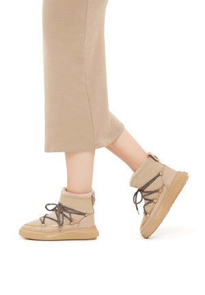 Beige insulated ankle boots with fur trim, textured fabric, lace-up design, and a ribbed rubber sole.