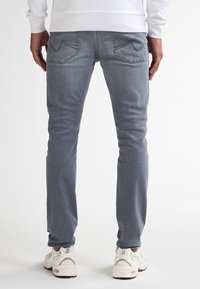Jeans skinny gri deschis din denim, cu două buzunare posterioare cu un design cusut, purtate cu adidași albi.