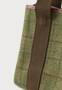 Πράσινη τσάντα από καρό ύφασμα με καφέ πλεχτό λουρί ώμου και λεπτομέρειες από δέρμα σε λευκό φόντο.