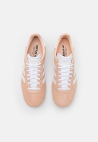 Zapatillas Adidas en ante melocotón con acentos en cuero blanco. Presentan tres rayas blancas, puntera redonda y cordones blancos.