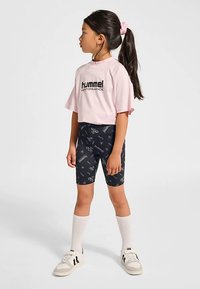 Rosa kort t-shirt med svart "Hummel Performance"-logotyp, kombinerad med mörka mönstrade cykelshorts och vita knästrumpor. Vita skor.