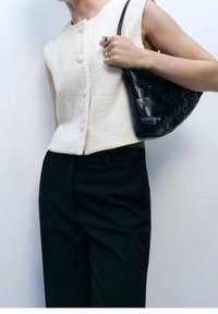 Biały, fakturowany top bez rękawów z przodu na guziki, zestawiony z czarnymi, dopasowanymi spodniami i plecioną czarną torebką.