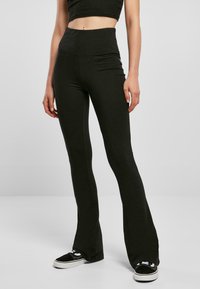 Leggings noires évasées avec une taille haute, fabriquées en matériau extensible, présentent une texture lisse et des coutures minimales pour le confort.