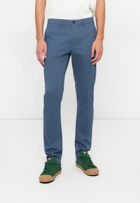 Light blue chinos made from cotton blend fabric, featuring a straight leg design and front pockets. Paired with green low-top sneakers.