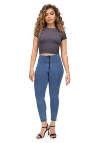 Crop top a coste di un grigio scuro abbinato a leggings in denim blu a vita alta con zip frontale e tacchi neri con cinghie.