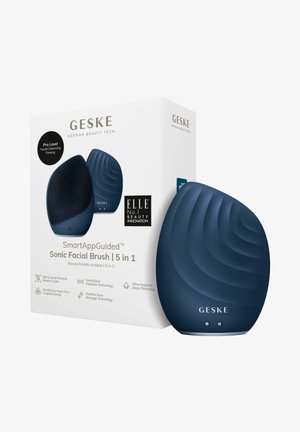 Sonic ansigtsbørste i navy blå, med ergonomisk design og bølgemønstret tekstur, inkluderer en æske med produktdetaljer og branding.