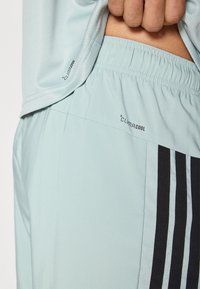 Shorts de sport bleu clair dotés d'un tissu respirant, d'une taille élastique et de bandes noires avec le logo « CLIMACOOL » imprimé sur le côté.