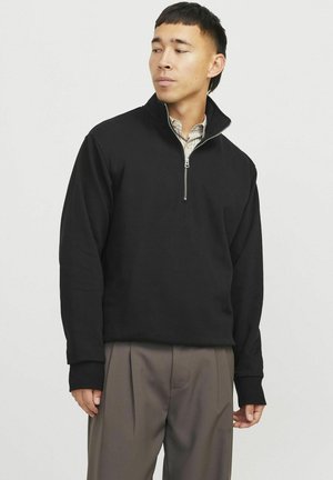 Felpa nera con zip, maniche lunghe, realizzata in tessuto testurizzato, dotata di un collo alto e polsini a costine. Abbinata a pantaloni grigi.