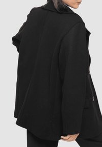 Abrigo de lana negro con un diseño estructurado, que presenta un cuello, botones grandes y un corte holgado, mostrando una tela suave y texturizada.