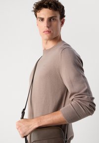 Pulover tricotat de culoare maro cu decolteu rotund și mansete cu model rib, asociat cu o geantă de umăr de culoare maro, cu o textură netedă și curea ajustabilă.