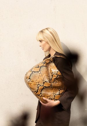 Große, ovalförmige Handtasche mit strukturierter Kunstschlangenprägung in Braun- und Gelbtönen, gehalten vor einer hellgrauen Wand.