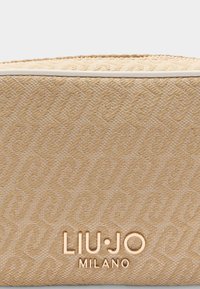 Beżowa tekstylna saszetka z plecionym wzorem, gładką fakturą i złotym logo "LIU·JO MILANO" na dole.