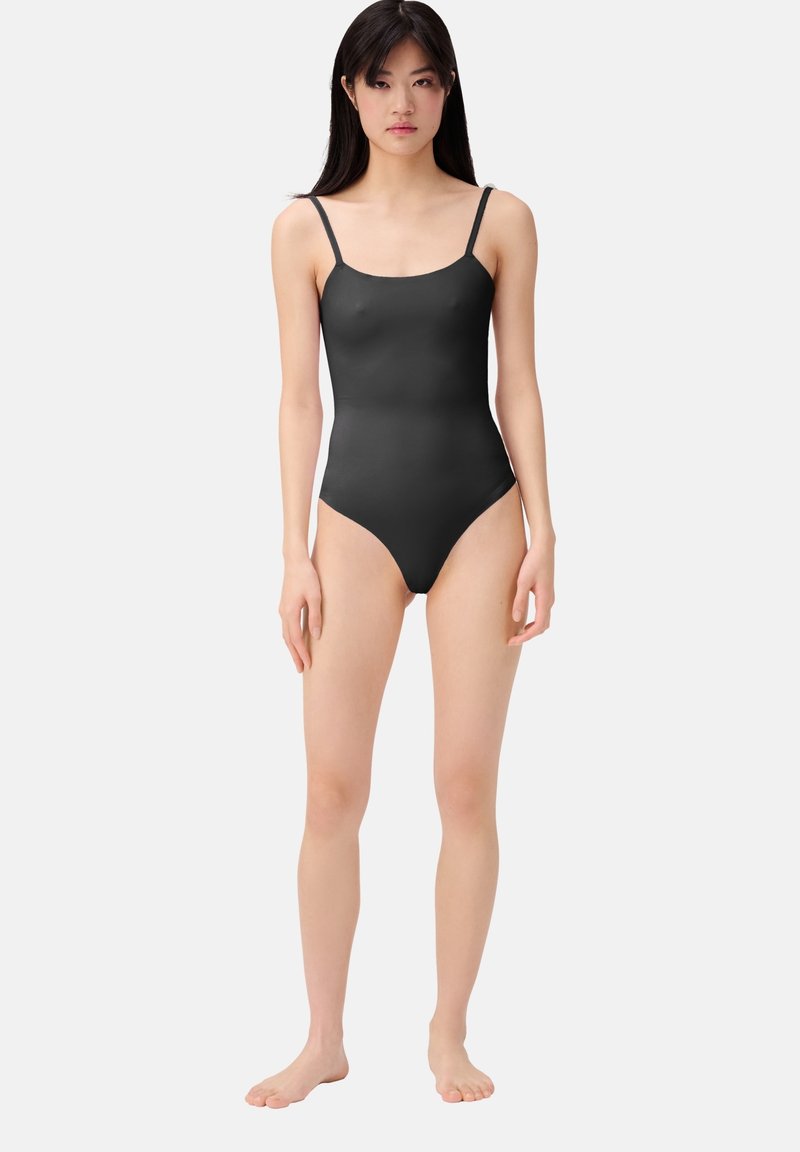Costume da bagno intero nero con spalline sottili, design aderente, texture liscia e aperture per le gambe ad altezza elevata.