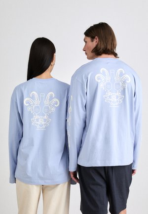 Les chemises à manches longues bleu clair sont ornées d'un design graphique blanc au dos, représentant des fleurs et des visages stylisés. Coupe décontractée, en coton.