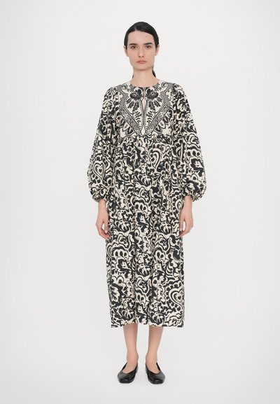 Schwarz-creamfarbenes Langarmkleid mit aufwendigem Paisleymuster, rundem Ausschnitt, elastischen Bündchen und fließender Silhouette. Schwarzfarbene Ballerinas inklusive.