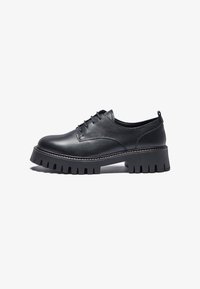 Chaussures en cuir noir avec un bout arrondi, un laçage et une semelle en caoutchouc épaisse et texturée avec des bords nervurés.