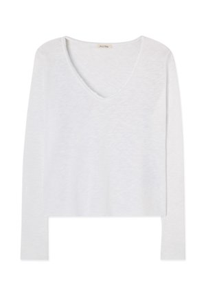 Balts kokvilnas tops ar garām piedurknēm un V veida izgriezumu, ar viegli teksturētu audumu un neapbruņotu kakla malu.