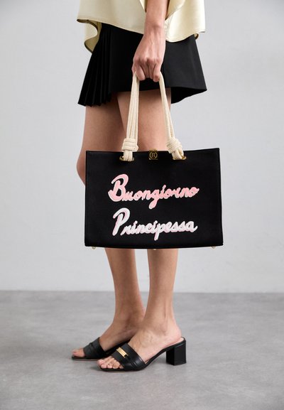 Black canvas tote bag with pink embroidered text "Buongiorno Principessa," featuring cream-colored rope handles and golden hardware accents.