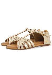 Sandalias metálicas doradas con diseño de barra T, punta abierta, múltiples correas frontales, hebilla ajustable en el tobillo y suela de goma marrón.