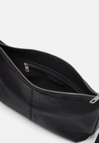 Schwarze Ledertasche mit silbernem Reißverschluss, die eine glatte Textur und eine Innentasche aufweist. Offenes Design, das das Innenleben und die Details des Markenlabels zeigt.