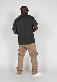 Tricou gri închis cu mâneci scurte, asortat cu pantaloni scurți bej din bumbac cu mai multe buzunare și o croială lejeră, purtați cu teniși albi.