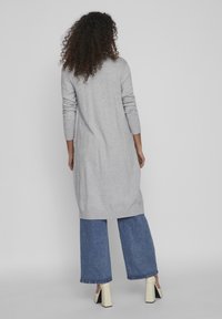 Lång grå tröja med ribbad nederkant och ärmslut, tillsammans med vida jeanstights. Outfiten inkluderar klumpiga vita högklackade skor.