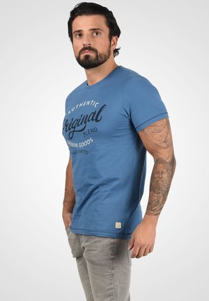 Modrá bavlnená tričko s textom "Original Blend Denim Goods" v čiernej farbe, okrúhly výstrih, krátke rukávy a malá nášivka na spodnom leme.