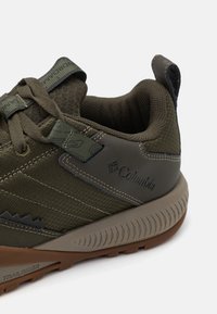 Buty trailowe Columbia w ciemnozielonym i szarym kolorze. Posiadają teksturowaną górę z siateczki, kontrastującą gumową podeszwę oraz logo po boku.