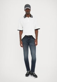 Λευκό πόλο μπλουζάκι με μαύρες λεπτομέρειες, στενά μπλε τζιν και μαύρα αθλητικά παπούτσια με λευκές λεπτομέρειες. Καθημερινό outfit με αθλητική διάθεση.