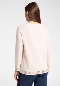Maglietta rosa chiaro a maniche lunghe con scollatura rotonda e decorazioni di perline lungo l'orlo e i polsini; texture liscia, vestibilità casual.