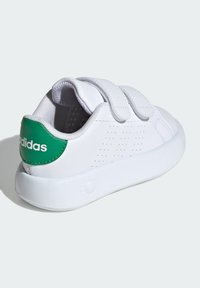 Zapatilla blanca con acento verde en el talón, que cuenta con dos correas de Velcro, diseño perforado y una suela de goma texturizada.