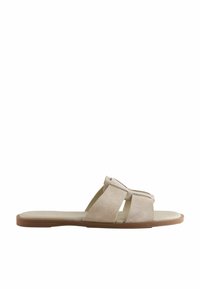 Beige mockasinsandal med öppen tå-design, två korsande remmar, en platt sula och en tan gummisula.