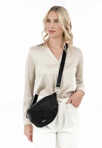 Black fabric crossbody bag with a curved design, zippered compartment, and adjustable strap. Suitable for casual use.