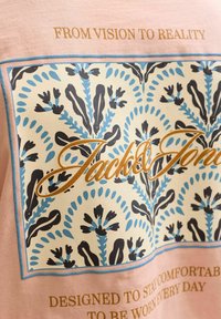 Κείμενο «Από το Όραμα στην Πραγματικότητα» και «Σχεδιασμένο να παραμένει άνετο για καθημερινή χρήση» σε ροζ ύφασμα με μπλε και μαύρο ανθικό μοτίβο.