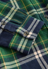 Flaneļa krekls ar zaļu, tumši zilu un baltu rūtainu rakstu. Mīksta tekstūra ar pogas aizdari un kontrastējošu apkakles detaļu.