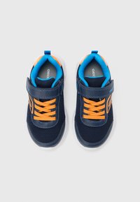 Tamsiai mėlynos tinklinės sportbačiai su oranžinėmis raištelėmis ir akcentais, su lipniomis juostelėmis, tekstūruota medžiaga ir baltu guminio padais.