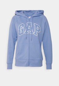 Haut de sweat bleu à zip avec une poche avant, capuche à cordon de serrage et logo "GAP" en lettres blanches contrastées. Tissu doux en mélange de coton.