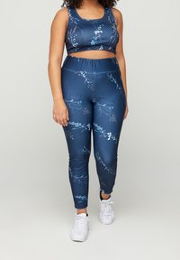Conjunto de ropa deportiva en azul marino que consiste en un top corto y leggings con patrones florales, hecho de una tela suave y elástica. Zapatillas blancas en la parte inferior.