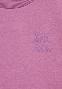 Ljubičasti dukserica od tkanine s rebrastim izrezom. Sadrži izvezeni logo "Dance" u nešto tamnijoj nijansi ljubičaste, okružen zvjezdicama.