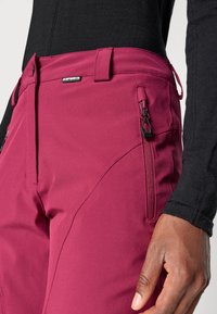 Magenta színű, slim fit szabású kinti nadrág. Jellemzői közé tartoznak a cipzáras zsebek, elegáns derékszíj és sima, enyhén texturált anyag.