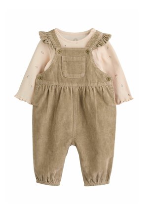 Peto de bebé de pana beige con tirantes fruncidos sobre una camiseta de manga larga color crema con pequeños estampados florales.