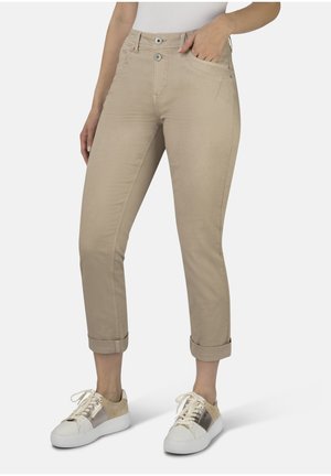 Beige Baumwollstretchhosen mit schlanker Passform, zwei Vordertaschen und umgeschlagenen Säumen, kombiniert mit weißen Sneakers mit goldenen Akzenten.