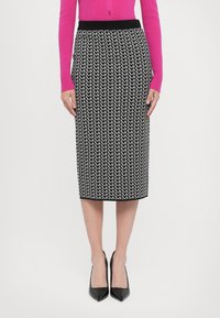 Schwarz-weiß gemusterter Bleistiftrock mit einem gestrickten Bund. Einfaches geometrisches Design und knielanger Schnitt. Getragen mit schwarzen Absatzschuhen.