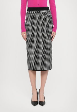 Jupe crayon à motifs noir et blanc avec une ceinture en tricot. Design géométrique simple et coupe mi-genoux. Portée avec des talons noirs.