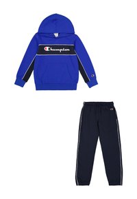 Sudadera azul con rayas horizontales en blanco y negro, que cuenta con un bolsillo tipo canguro y un logo. Complementada con pantalones jogger negros con ribete blanco.