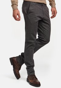 Pantalons gris texturé avec une coupe ajustée, poches latérales et passants de ceinture, associés à des bottes en cuir marron à lacets et un pull en tricot contrastant.