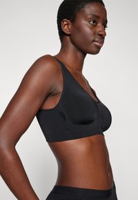 Black wireless bra with adjustable straps, featuring a soft, stretchy fabric and a smooth texture. V-neck design enhances comfort.