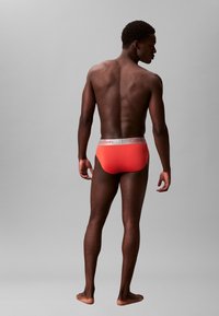 Calvin Klein Herrenunterhosen in leuchtendem Koralle mit einem weißen Logo-Bund. Weicher Stoff mit einer engen Passform, von hinten sichtbar.