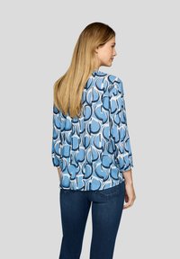 Blaue gemusterte Bluse mit Dreiviertelärmeln, die abstrakte Formen in helleren Farbtönen zeigt und aus einem glatten, leichten Stoff gefertigt ist.