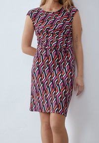 Robe à motifs avec des manches courtes, présentant des formes géométriques en rouge, rose et blanc sur un fond noir. Ajustée avec des fronces à la taille.